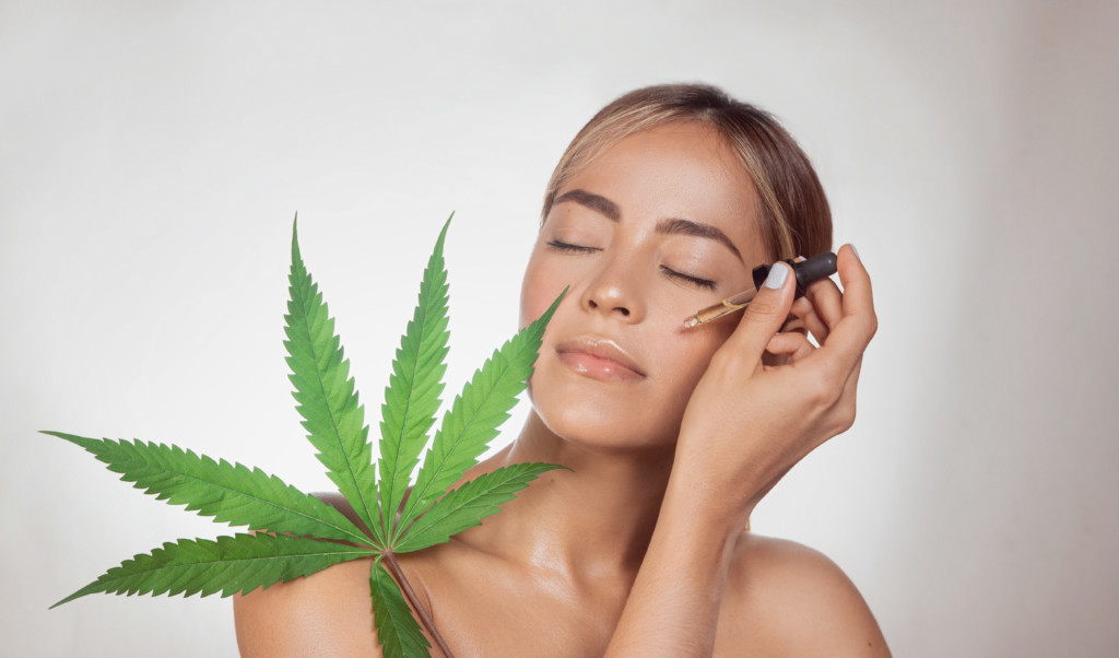 大麻草とCBDオイルを顔に塗る女性